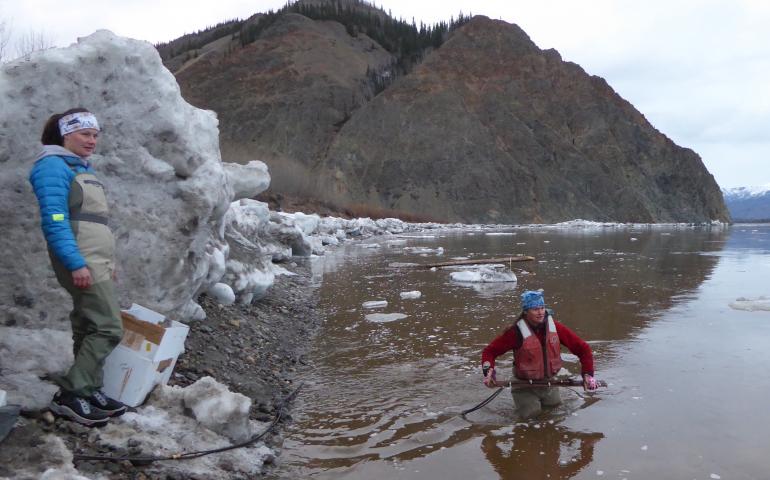 Heather Best (in water), a USGS hydrologist, prepares to toss a road-grader blade with a river-measuring device attached into the Yukon River near Eagle, Alaska. USGS hydrologic technician Liz Richards watches for ice. Photo by Ned Rozell.