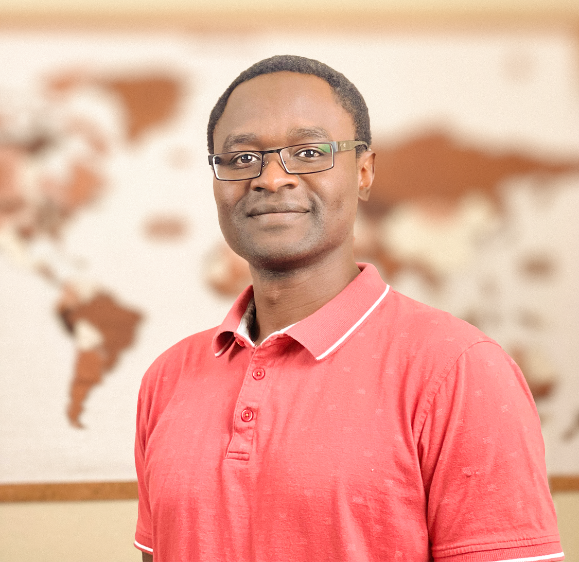 pictured - speaker Evans Onyango in a salmon colored polo shirt and clean rimmed glasses smiling and standing in front of a Earth-tone colored world map