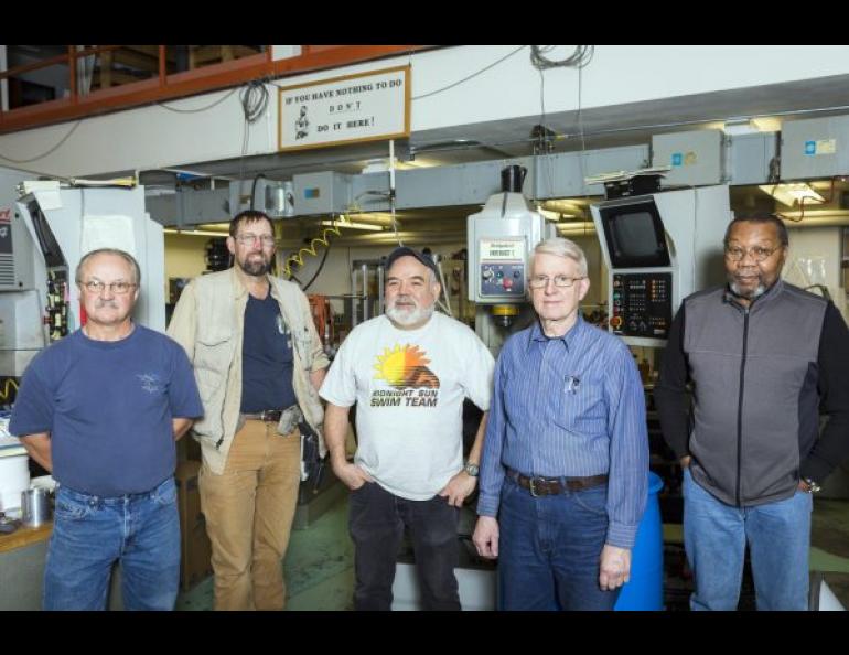 Geophysical Institute Machine Shop staff members, from left, Kurt Laiti, Dale Pomraning, Jesse Atencio, Phil Woodard and shop manager Greg Shipman, below a sign stating that “If you have nothing to do, don’t do it here!” Former shop manager Larry Kozycki installed the sign. UAF photo by JR Ancheta.