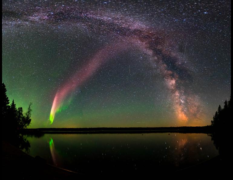 The Strong Thermal Emission Velocity Enhancement, visible as a pink band rising from the lower left to upper right of this photograph, appears with the Milky Way over Childs Lake, Manitoba, Canada. Image courtesy of Krista Trinder and NASA