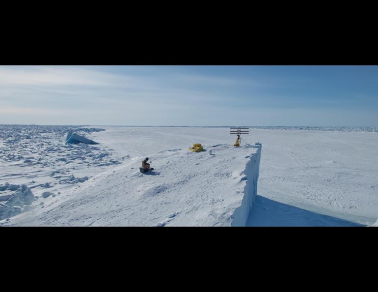 Graduate student researcher Emily Fedders sits on top of an ice island with the portable interferometric radar. The ice island is in landfast sea ice on Alaska’s Arctic coast near Utqiaġvik. Photo courtesy of Andy Mahoney.