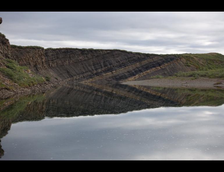 Part of the Nanushuk Formation, visible as a darker slanted rock layer, rises in a bluff above a bend of the Kukpowruk River. A large number of dinosaur tracks were found in this area. Photo courtesy of Anthony Fiorillo