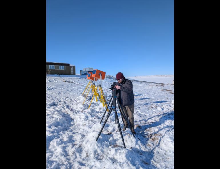 Graduate student researcher Austin Smith looks through one of three UAF cameras set up as part of the AWESOME mission. Orange enclosures on yellow tripods house cameras of Clemson University, which is a partner in the UAF-led AWESOME mission. Photo by Cameron Westerlund