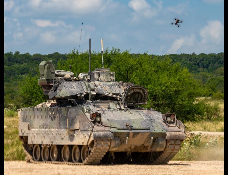 A small quadcopter unmanned aircraft system hovers above an M2 Bradley Infantry Fighting Vehicle on a dirt training range at Fort Hood, Texas, with trees in the background. The scene, captured Aug. 27, 2025, during Operation Return of the Condor, shows the drone positioned overhead in a test.