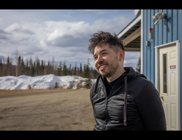 Juan Camilo Buitrago-Casas of the University of California, Berkeley stands outside the payload assembly building at Poker Flat Research Range, speaking about the FOXSI-5 mission he leads. He smiles while facing slightly to the side, with snowbanks, trees and a partly cloudy sky in the background.