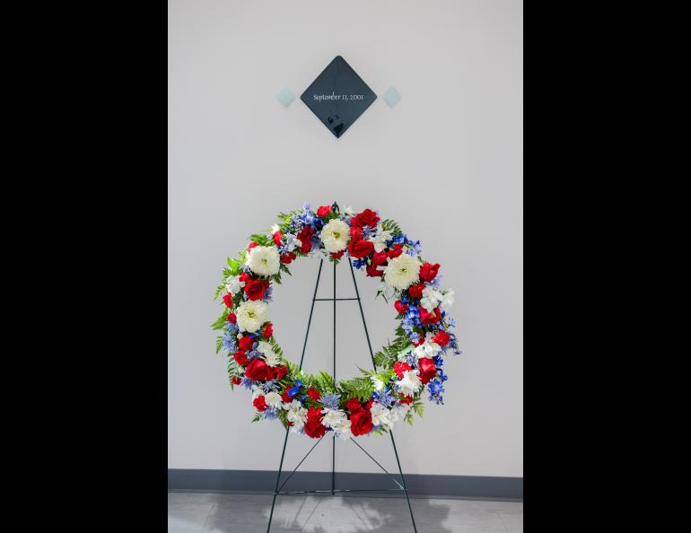 A wreath of red, white and blue flowers is on a stand below the tile commemorating 9/11.