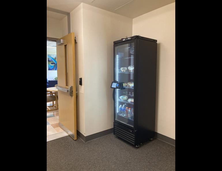 A tall vending machine with refrigerated food items stands in a corner. 