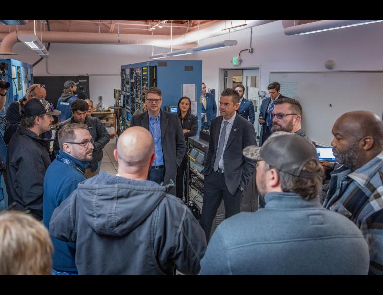 A group of people stand in a group in a room with racks of electronic equipment in the background