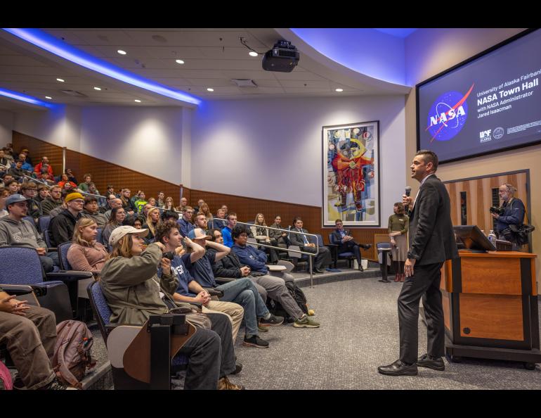 A man with a microphone speaks to a room full of people