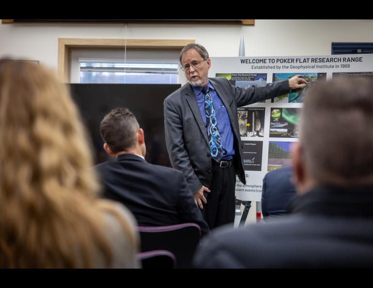 A man points to a picture on a stand while people are listening
