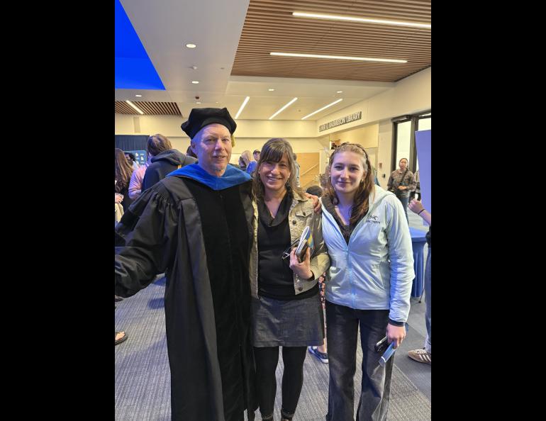 Ned, Kristen and Anna Rozell stand together in the UAF Great Hall's building lobby. Ned is dressed in UAF regalia after being awarded the AF Gold Ceremony on May 1, where Ned was awarded Science Writer Emeritus.