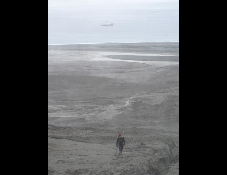 Jeff Williams, a biologist with the Alaska Maritime National Wildlife Refuge, hikes a muddy slope of Kasatochi Island with the refuge ship Tiglax in the background. Photo by Ned Rozell.