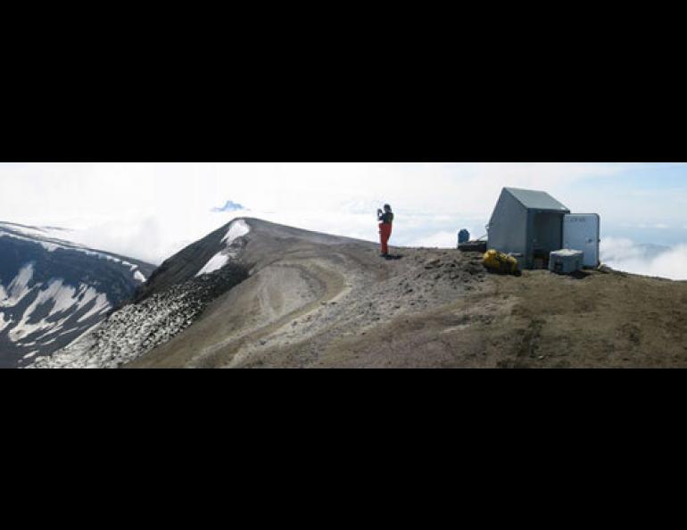  The gray fiberglass hut in which the Alaska Volcano Observatory’s Guy Tytgat spent a miserable night on Okmok Caldera. Here, in better weather, Jackie Caplan-Auerbach is pictured in 2002. Photo by Guy Tytgat. 