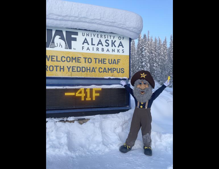 Alaska Goldpanners baseball team mascot Happy Boy (aka Chris Carlson of Fairbanks) poses in front of the University of Alaska Fairbanks temperature sign on the morning of March 1, 2026. Photo by Ned Rozell.
