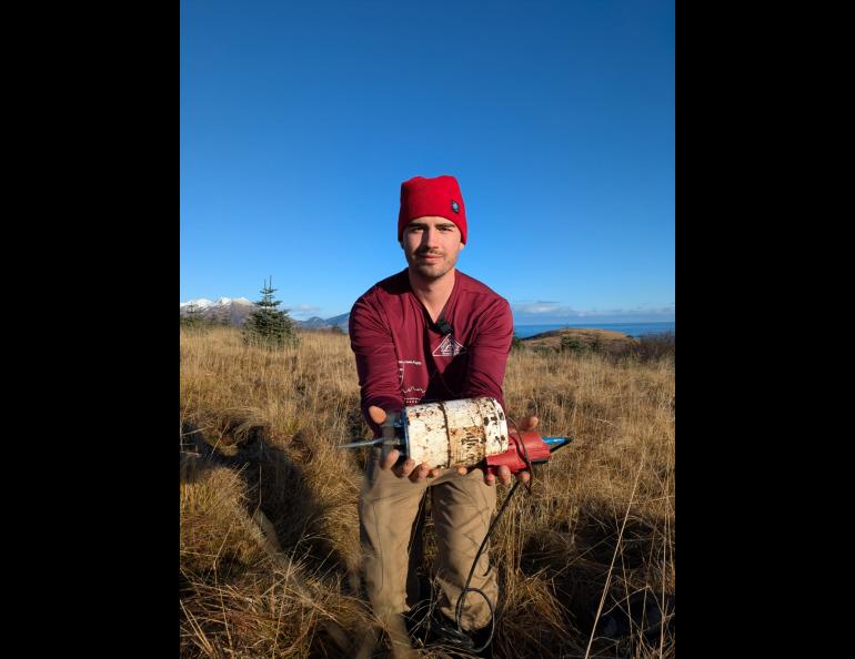 University of Alaska Fairbanks doctoral student Cade Quigley holds a freshly unearthed seismic sensor in Kodiak in November 2025. Photo by Sara Wilbur