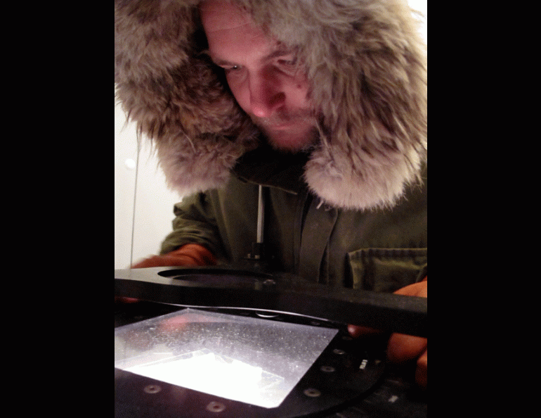 Dressed for the below-zero Fahrenheit temperature of a cold room, Marc Mueller-Stoffels looks at a thin slice of sea ice through a polarizing filter. Ned Rozell photo.