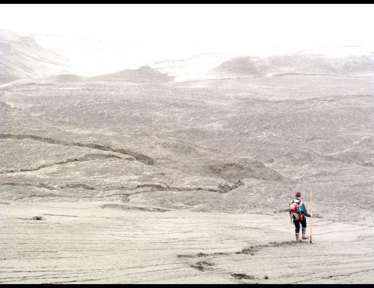 Picture of a scientist hiking among the sand with a mountain in the background.