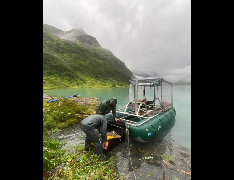 Drake Singleton, left, and Peter Haeussler install a sound wave-generating device onto a pontoon boat they carried to Allison Lake near Valdez. Photo by Gerry Hatcher.