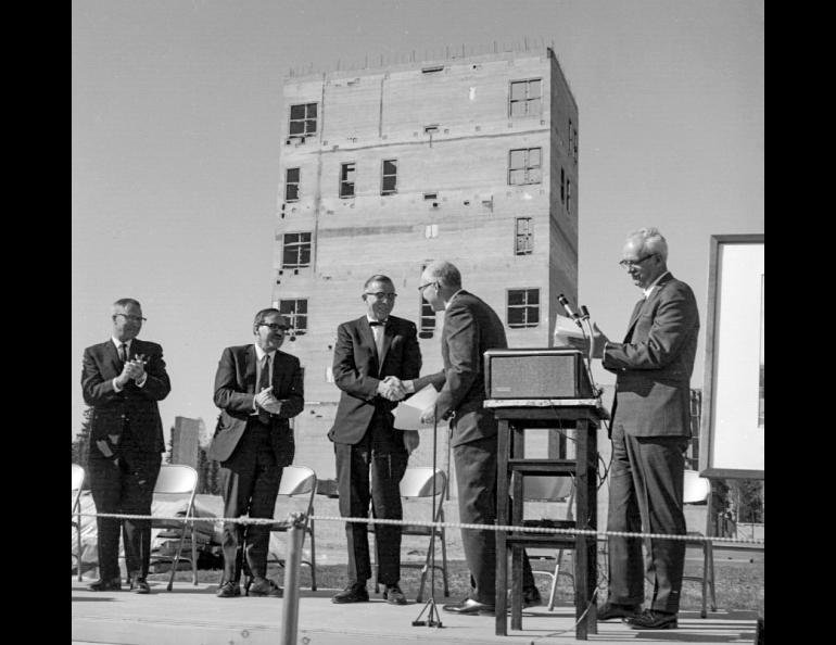 People shaking hands and clapping in front of a partially-constructed building