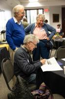 Tom Hallinan (seated) reviews a photo while Hans Nielsen (left) and Nancy Hallinan look on at the 2026 GI reunion. Photo by Tucker Forbes