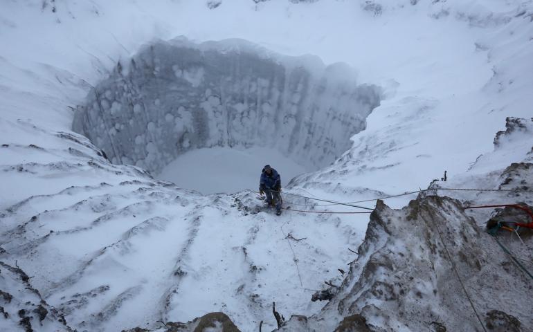 A member of an expedition group stands on the edge of a newly formed crater on the Yamal Peninsula in northern Siberia in November 2014. Photo by Vladimir Pushkarev, Reuters via Nova