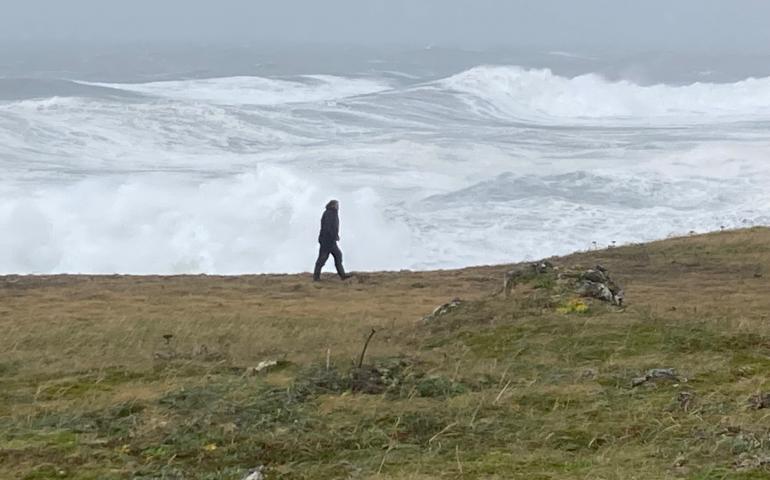Filmmaker Fritz Mueller walks at the edge of St. Paul Island as waves crash ashore, driven by the remnants of Typhoon Merbok as it passes over St. Paul Island. Photo by Chris Maio