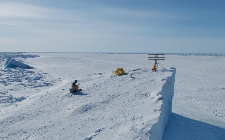 Graduate student researcher Emily Fedders sits on top of an ice island with the portable interferometric radar. The ice island is in landfast sea ice on Alaska’s Arctic coast near Utqiaġvik. Photo courtesy of Andy Mahoney.