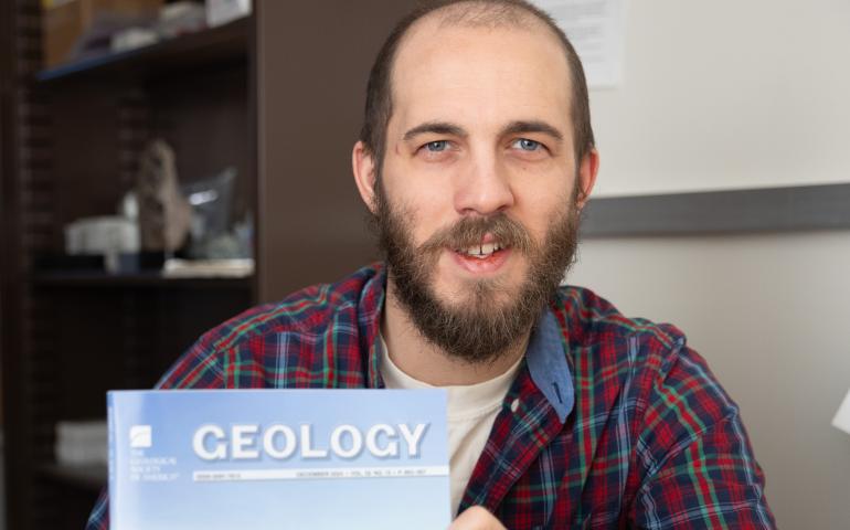 Associate professor Sean Regan holds a copy of the December edition of Geology, which features his latest research in its cover photo. Photo by Bryan Whitten