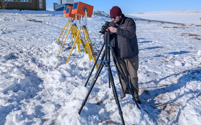 Graduate student researcher Austin Smith looks through one of three UAF cameras set up as part of the AWESOME mission. Orange enclosures on yellow tripods house cameras of Clemson University, which is a partner in the UAF-led AWESOME mission. Photo by Cameron Westerlund