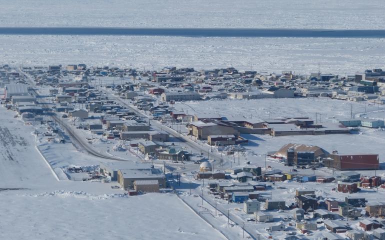 Aerial view of Utqiaġvik, Alaska, showing a snow-covered coastal town bordered by sea ice. A long, narrow strip of open water called an open flaw lead cuts across the frozen ocean, separating the solid landfast ice attached to shore from the drifting pack ice offshore. Photo by Andrew Mahoney