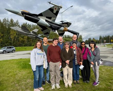 Several people stand in front of a mounted jet fighter.