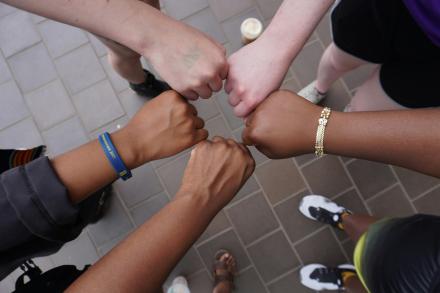 Five hands of five different people join in the middle to create a star