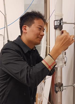 A man is standing, making an adjustment to a white column he's stanading next to