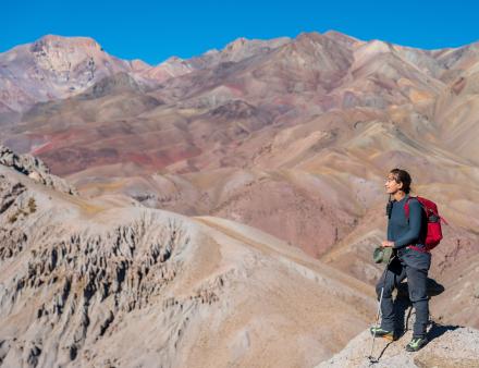 A woman hiking in the mountains smiles as she looks off into the distance.