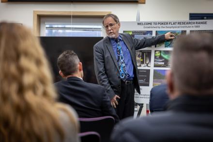 A man points to a picture on a stand while people are listening