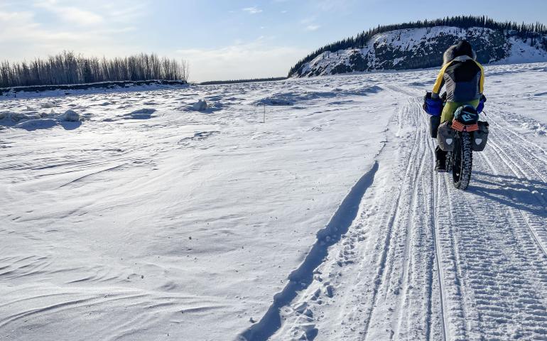 Forest Wagner rides his fat bike near Bishop Rock, right, a pinch point on the flow of the Yukon River, on April 5, 2026. Photo by Ned Rozell.
