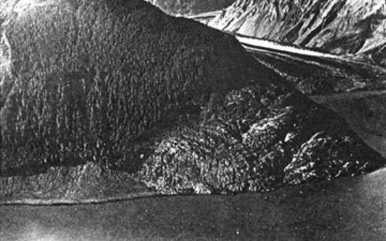 Headland beside the Lituya Glacier that was swept clean of soil and trees to a height of 1740 feet by the giant splash wave. The icebergs seen in the water of Lituya Bay, foreground, were knocked off the glacier by the landslide falling into the bay from a slope to the right of the photograph. Photo by Byron Hale.