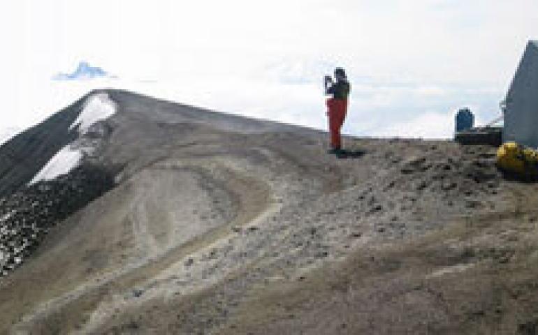  The gray fiberglass hut in which the Alaska Volcano Observatory’s Guy Tytgat spent a miserable night on Okmok Caldera. Here, in better weather, Jackie Caplan-Auerbach is pictured in 2002. Photo by Guy Tytgat. 