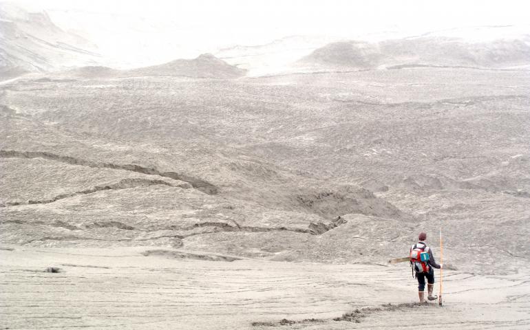 Picture of a scientist hiking among the sand with a mountain in the background.