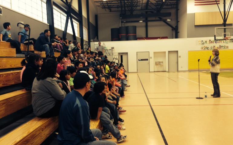 Natalia Rupport speaking to those assembled in the Noatak school gym at night, describing earthquakes and aftershocks.