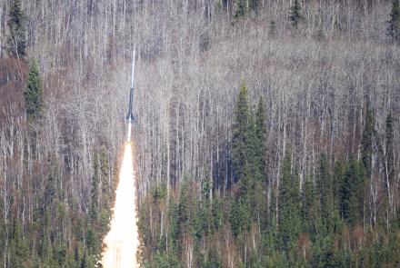 A NASA sounding rocket carrying the FOXSI-5 mission lifts off from Poker Flat Research Range north of Fairbanks at 11:23 a.m. Thursday, May 14, 2026. A bright plume of flame and smoke rises from the launch pad as the rocket climbs above a dense forest of spruce and leafless birch trees.