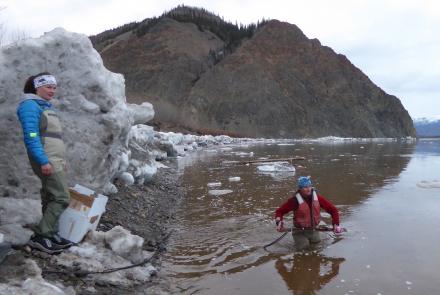 Heather Best (in water), a USGS hydrologist, prepares to toss a road-grader blade with a river-measuring device attached into the Yukon River near Eagle, Alaska. USGS hydrologic technician Liz Richards watches for icebergs. Photo by Ned Rozell.