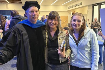 Ned, Kristen and Anna Rozell stand together in the UAF Great Hall's building lobby. Ned is dressed in UAF regalia after being awarded the AF Gold Ceremony on May 1, where Ned was awarded Science Writer Emeritus.